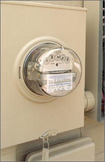 A photo of an electric meter contained in a beige metal box with the meter gauges displayed through a glass bowl-like covering. 