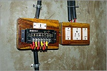 A photo of a charge controller. The charge controller—two rectangular-shaped boxes with switches and small, round indicator lights—has wiring running to and from it. 